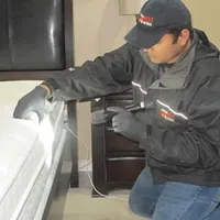 Bed bug inspection technician checking a mattress and bed frame for signs of infestation in {city}, {state}